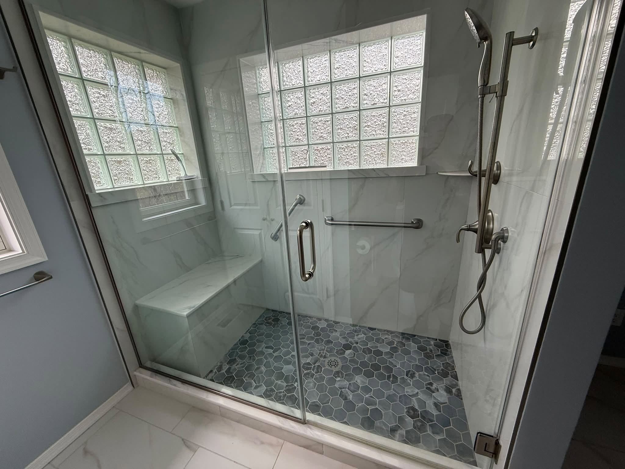 Glass-enclosed custom shower with tiled bench and hexagon floor